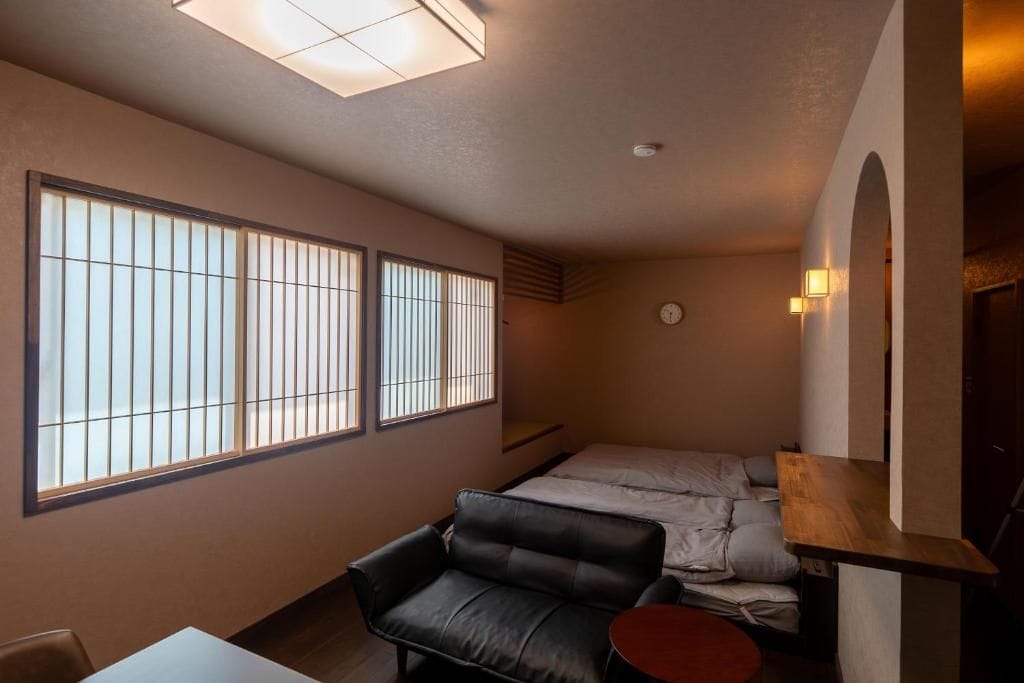 Una habitación compacta con cama, sofá, una mesita y estantería en la pared.