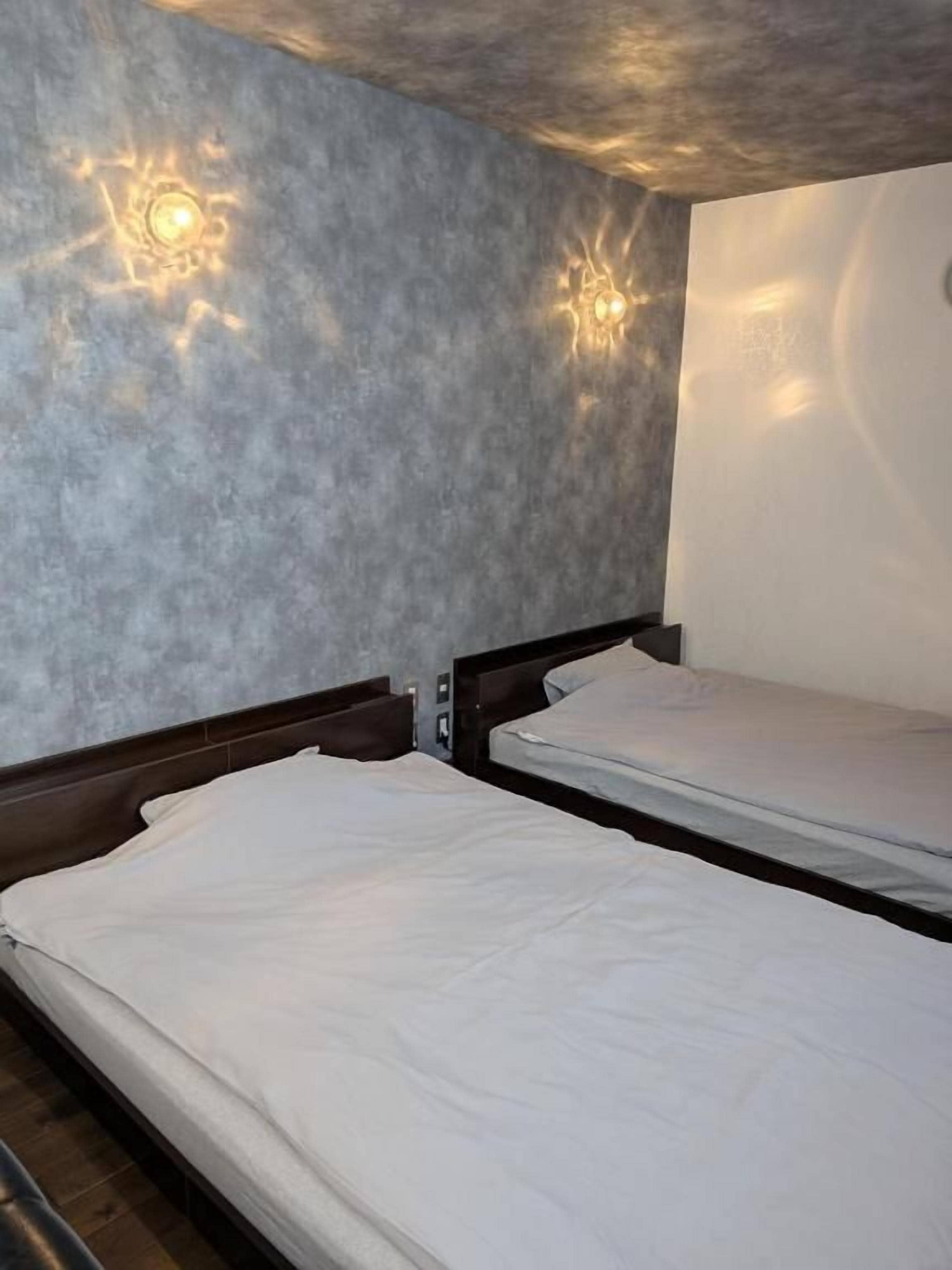 A room with two beds, a concrete wall, and a light fixture.