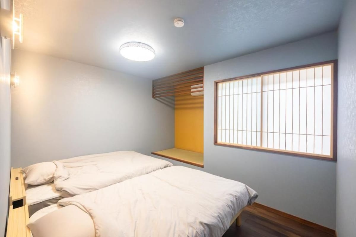 A bedroom with two beds, a window with bars, a ceiling light, and a wooden bench.