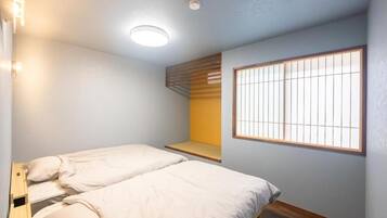 Een slaapkamer met twee bedden, een raam met tralies, een plafondlamp en een houten bankje.