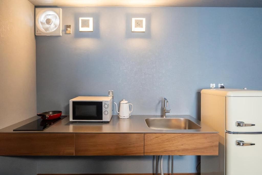 A compact kitchenette with a microwave, kettle, sink, and a small refrigerator.