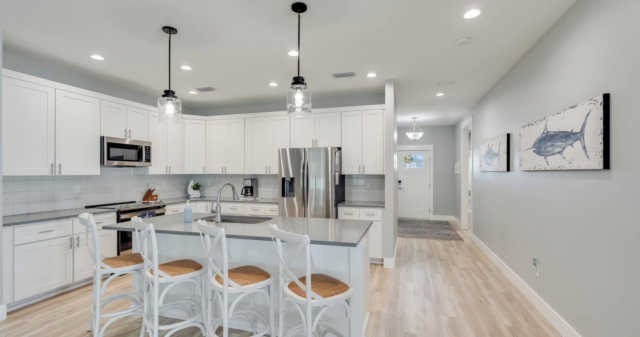 A modern kitchen with white cabinetry, stainless steel appliances, and a central island with bar stools.