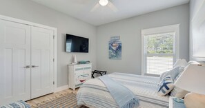 Ein Schlafzimmer mit einem Bett, einem Schminktisch, einem Fernseher, einem Fenster mit Jalousien und einem Deckenventilator.