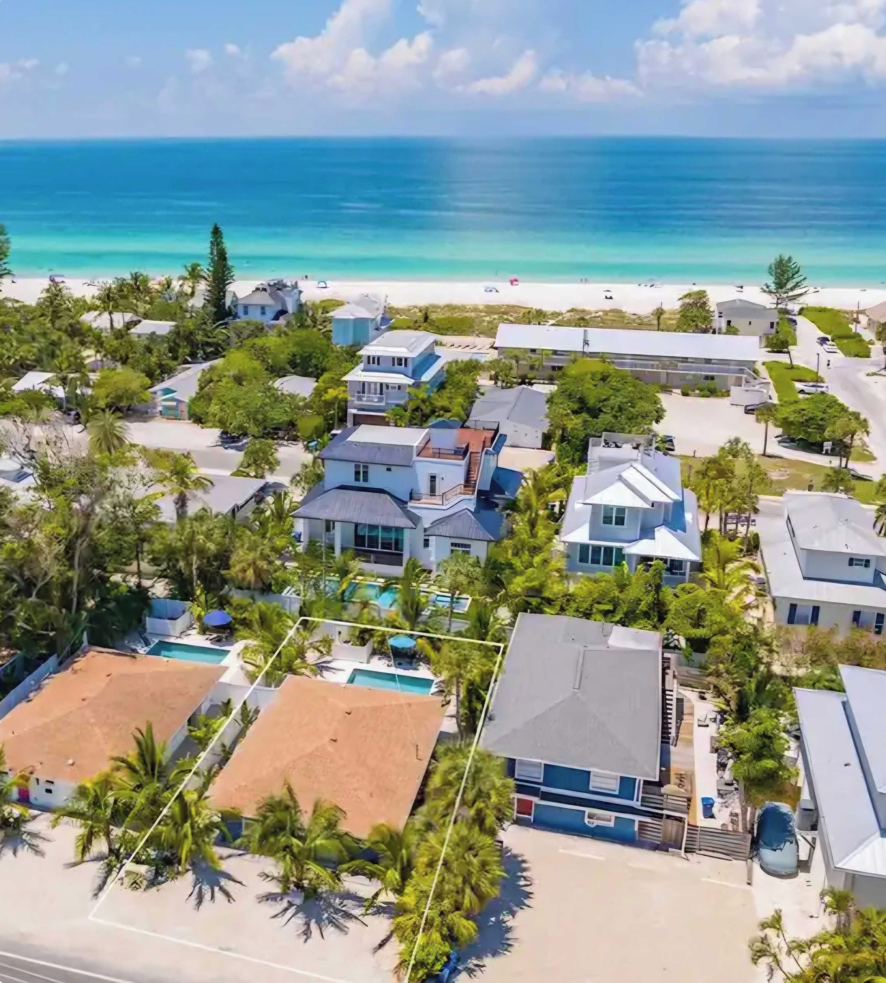 A coastal residential area with houses, a swimming pool, and a beach in the background.