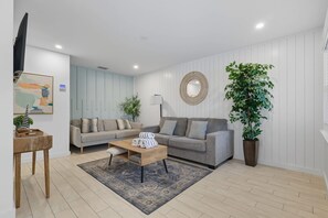 Ein Wohnzimmer mit einer Sofagarnitur, einem Couchtisch, einem Teppich, einer Topfpflanze und einem an der Wand befestigten Spiegel.