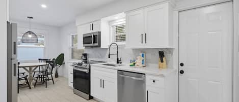 Cocina moderna con armarios blancos, electrodomésticos de acero inoxidable y un comedor con mesa y sillas.