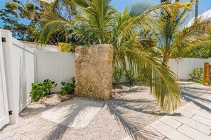 A garden with palm trees, a concrete planter, and a white fence. - Steps from Beach & Trolley|Heated Pool&Spa Duplex (Holmes Beach)