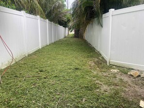 A narrow pathway flanked by white fences, with grass and small rocks on the ground. - Steps from Beach & Trolley|Heated Pool&Spa Duplex (Holmes Beach)