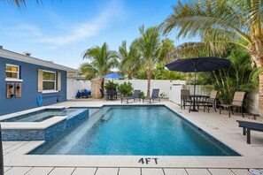 A rectangular swimming pool with a 4FT depth marker, surrounded by lounge chairs and umbrellas, with palm trees in the background. - Steps from Beach & Trolley|Heated Pool&Spa Duplex (Holmes Beach)