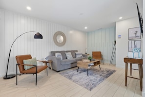 A modern living room with a grey sofa, two brown armchairs, a coffee table, a floor lamp, and a decorative mirror. - Steps from Beach & Trolley|Heated Pool&Spa Duplex (Holmes Beach)