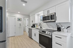 A modern kitchen with white cabinetry, a stainless steel refrigerator, a microwave, a stove, and a coffee maker. - Steps from Beach & Trolley|Heated Pool&Spa Duplex (Holmes Beach)