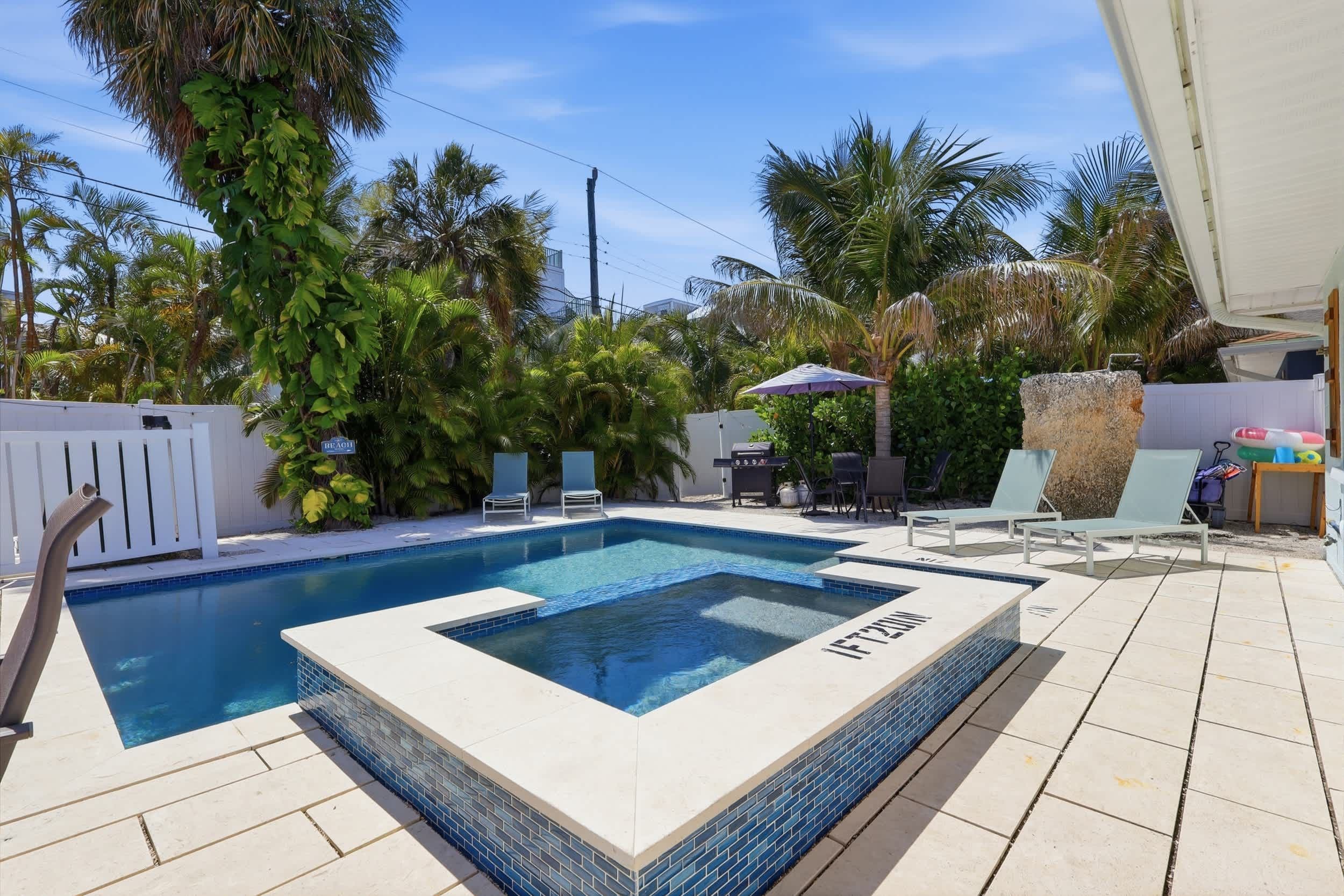 Ein rechteckiger Pool mit einer Fliesenbordsteinkante, umgeben von Liegestühlen und einem weißen Zaun.
