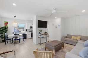 Ein modernes Wohnzimmer mit einer Couch, einem Hocker und einem Essbereich mit Stühlen und einem Tisch.