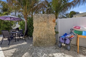 Un patio al aire libre con una mesa, sillas, una parrilla, una palmera y una valla blanca.