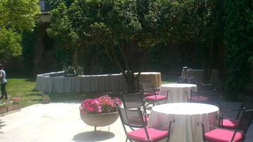 Une terrasse extérieure avec des tables et des chaises rondes, entourée de verdure et d’un mur de pierre.