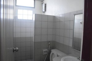 Une salle de bain carrelée de blanc, avec des toilettes, un espace douche et une fenêtre laissant entrer la lumière naturelle.