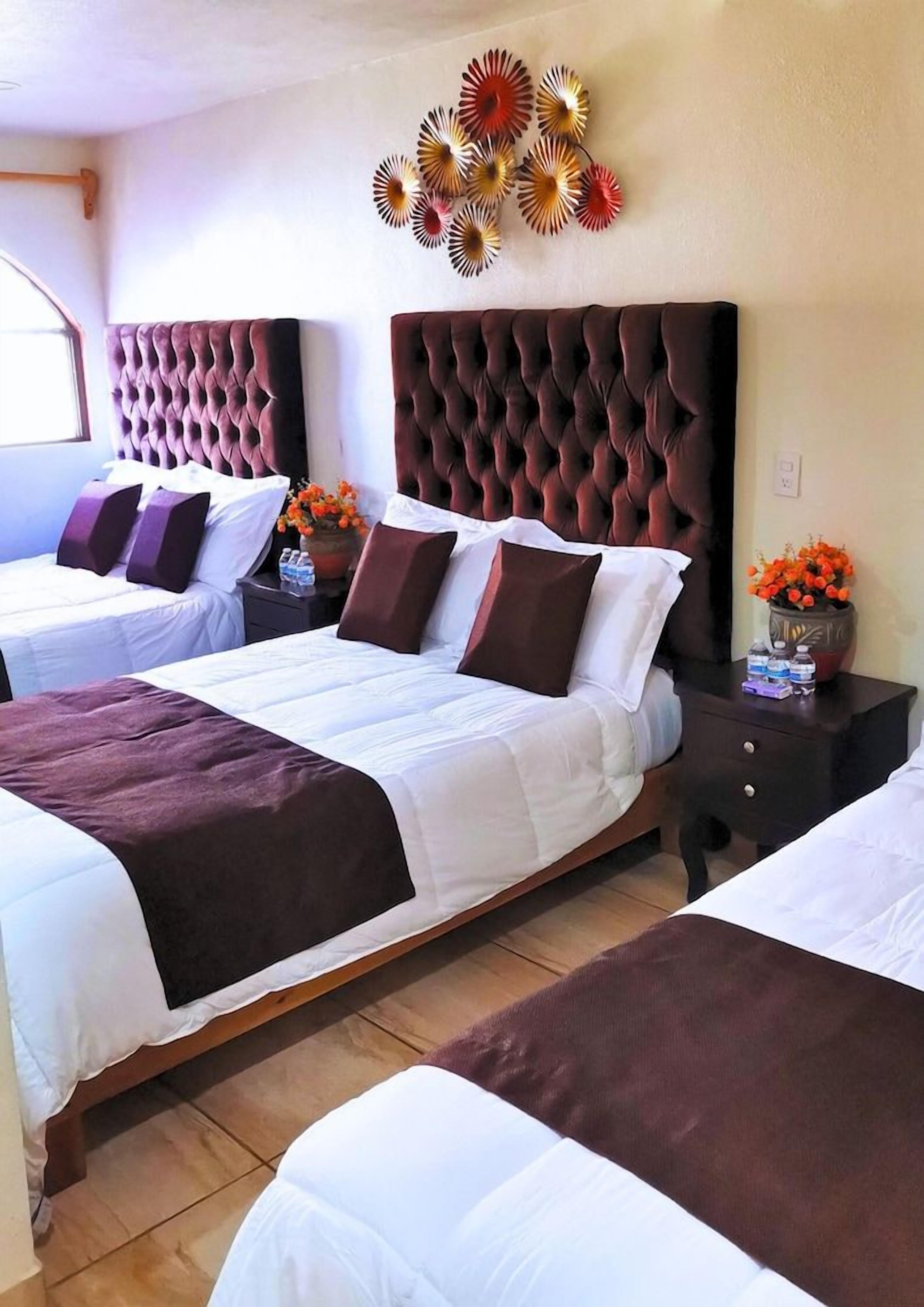 Ein Hotelzimmer mit zwei Betten, einem Wandbild und einem Nachttisch mit Blumen.