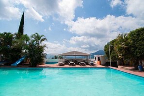 A swimming pool with lounge chairs and a shaded area, surrounded by palm trees and a clear sky. - Resort y Balneario Los Angeles (Taxco)
