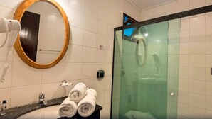 A bathroom with a round mirror, a hairdryer, a glass shower enclosure, and towels on the counter. - Pousada Sarata Tartaruga (Búzios)