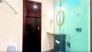 Un baño con puerta de madera oscura, separador de vidrio, espejo y un inodoro.
