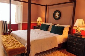 A four-poster bed with a tufted bench, two bedside tables with lamps, and a mirror on the wall. - Belo Monte Hotel and Museum (Príncipe Island)