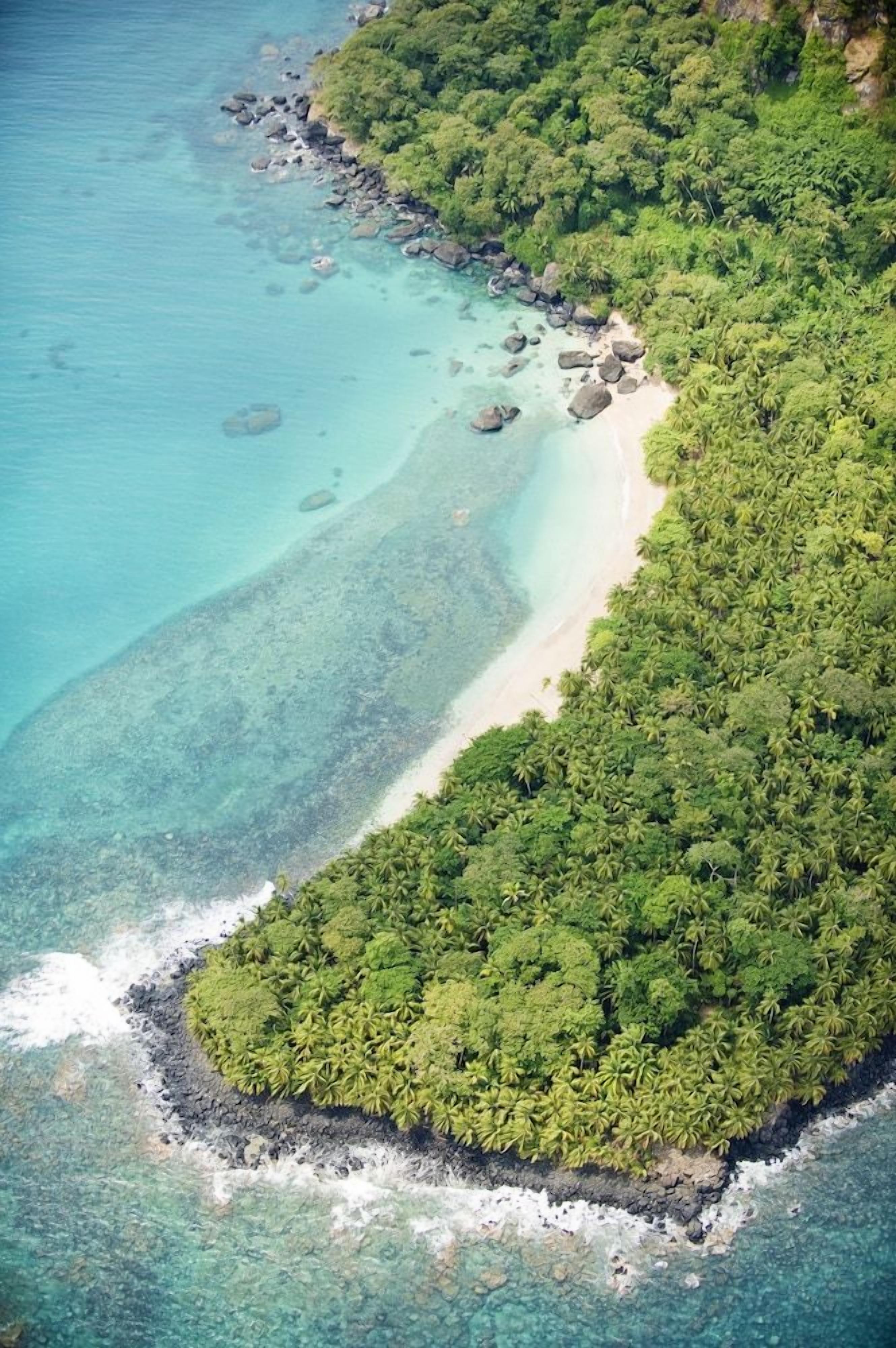Vista aérea de una isla tropical con playa, aguas turquesas cristalinas y densa vegetación verde.