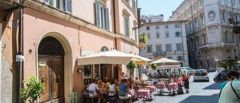 An outdoor café with tables and chairs, a potted plant, and a building with a sign.