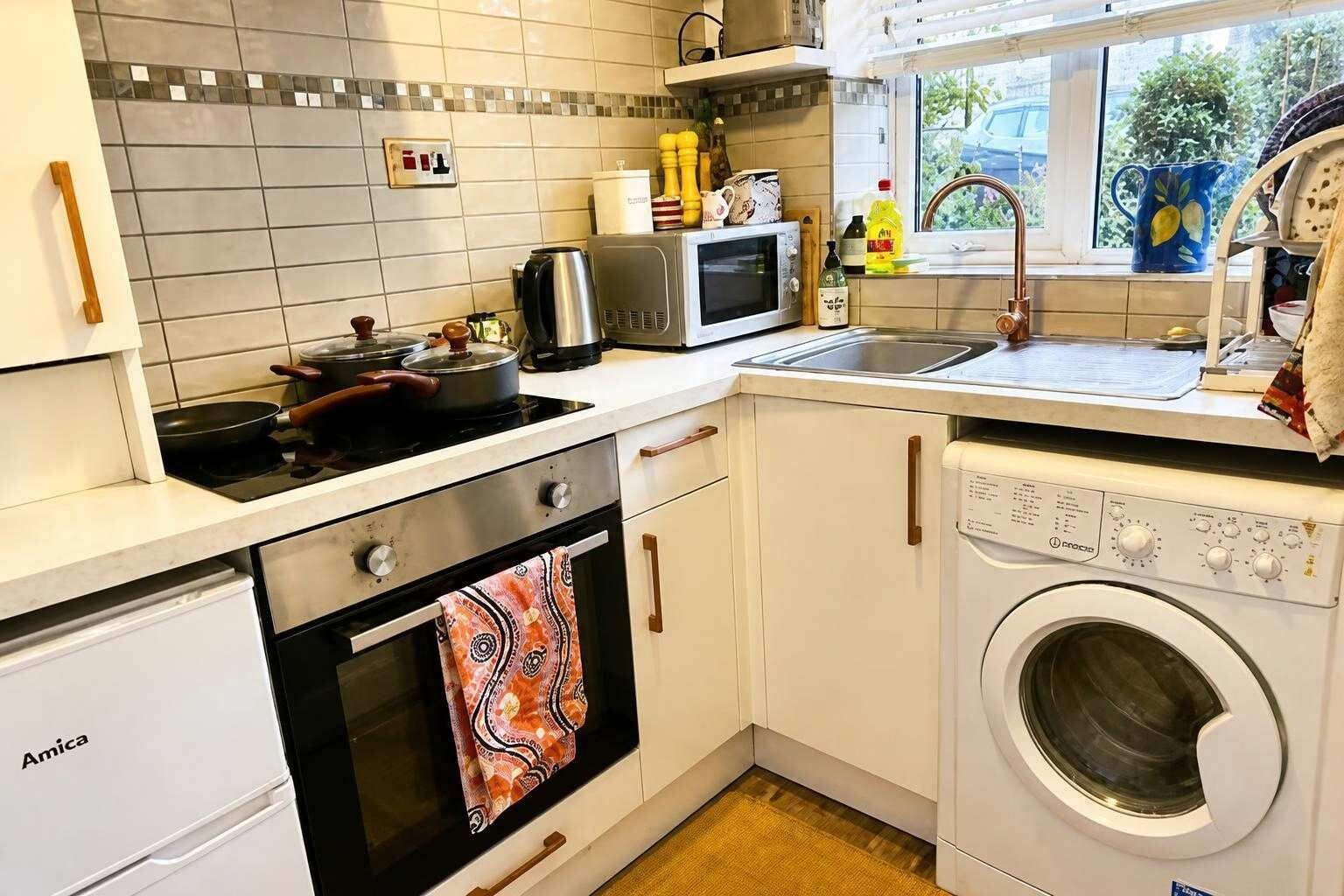 A compact kitchen with an oven, microwave, sink, and washing machine.