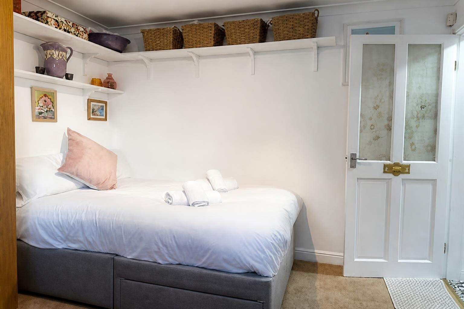A bedroom with a bed, pillows, a bedside table, a wardrobe, and a door with a handle.