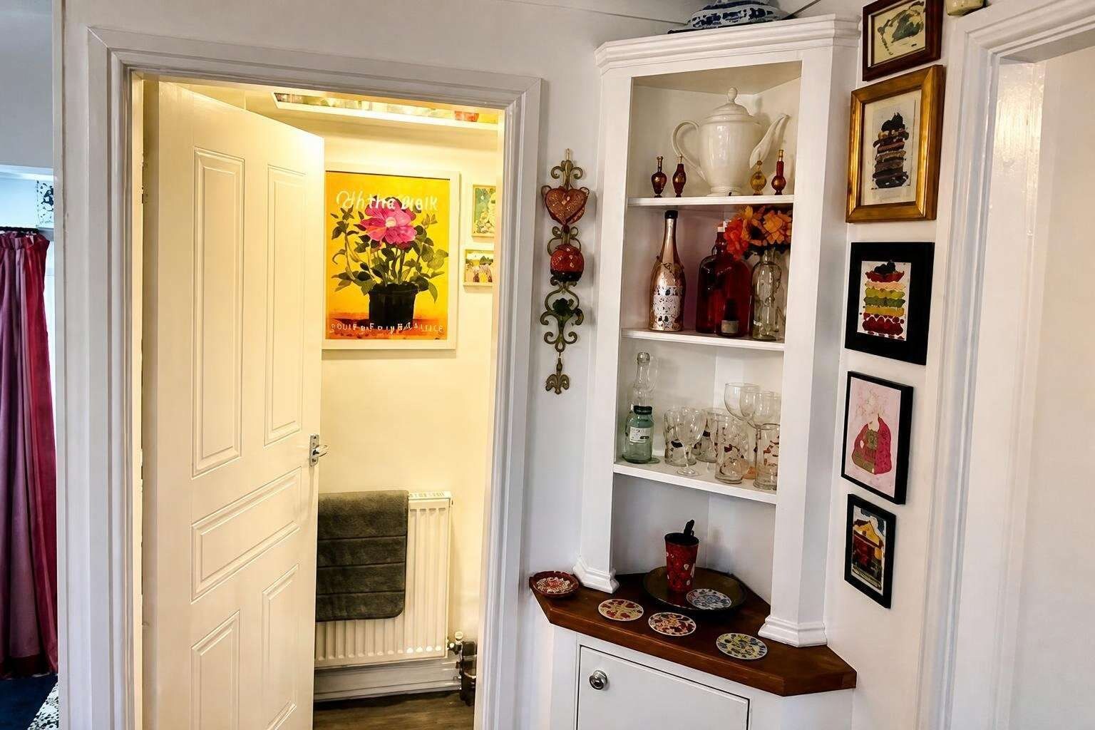 Un pasillo con una puerta blanca, un radiador, una repisa con adornos y un cuadro en la pared.