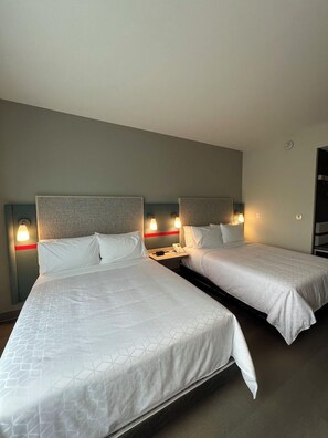 A hotel room with two beds, each with a headboard, bedside tables, and wall-mounted lamps. - Avid Hotels Guadalajara Av Vallarta Pte (Zapopan)