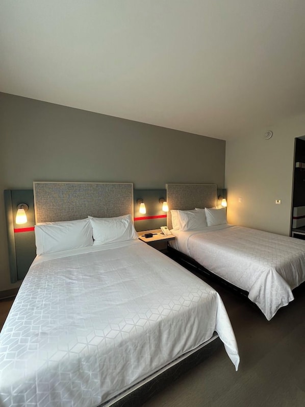 A hotel room with two beds, each with a headboard, bedside tables, and wall-mounted lamps. - Avid Hotels Guadalajara Av Vallarta Pte (Zapopan)
