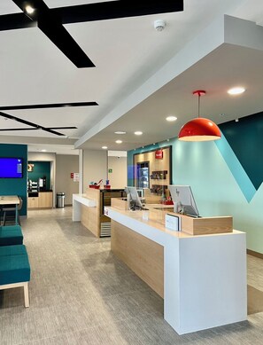 A modern reception area with a wooden counter, a red pendant light, and a teal accent wall. - Avid Hotels Guadalajara Av Vallarta Pte (Zapopan)