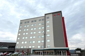 Ein modernes Hotelgebäude mit einer markanten roten und grauen Fassade, zahlreichen Fenstern und einem gut sichtbaren Eingang.