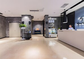A modern hotel lobby with a reception desk, a seating area with a plant, and a fireplace. - Echarm Hotel (Fuzhou)