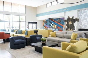 Ein moderner Lounge-Bereich mit Sofas, Sesseln und einem Couchtisch, mit einem großen Fenster und abstrakter Wandkunst.