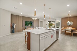 Een moderne keuken met een centraal eiland, hanglampen en een eethoek met een houten tafel en stoelen.