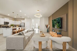 A modern living room with a sectional sofa, a coffee table, and a TV mounted on the wall. - 8BR Windsor Cay villa with private pool, game room, sleeps 16 (Clermont)