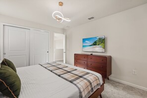 A bedroom with a bed, a dresser, a television on the wall, and a door. - 8BR Windsor Cay villa with private pool, game room, sleeps 16 (Clermont)
