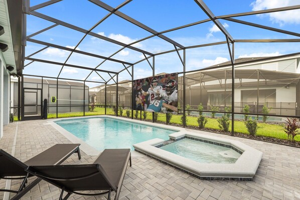 Een zwembad met ligbedden, een jacuzzi en een groot scherm waarop een sportevenement wordt getoond.