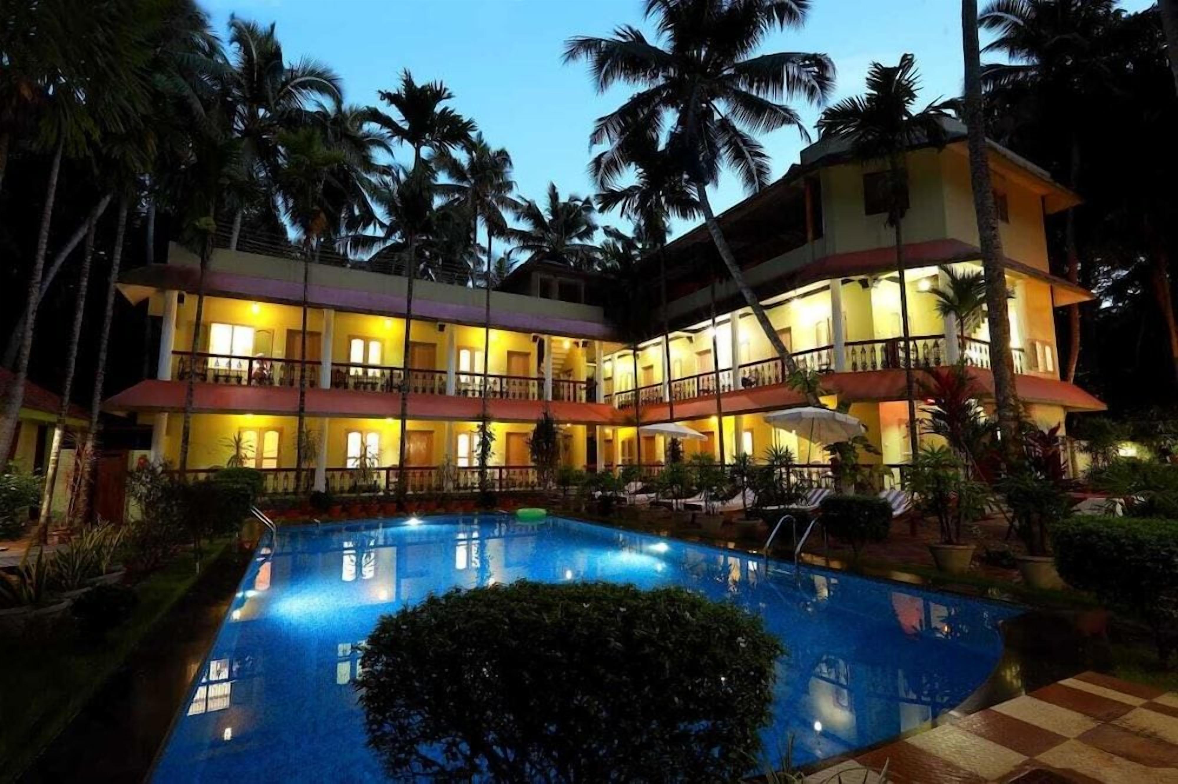 A hotel with a swimming pool, multiple balconies, and palm trees.