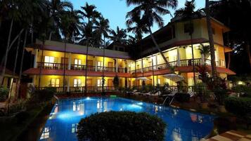 A hotel with a swimming pool, multiple balconies, and palm trees.