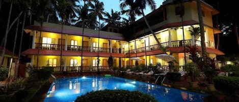 Um hotel com piscina, várias varandas e palmeiras.