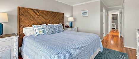 Een slaapkamer met een bed, een houten hoofdbord, een plafondventilator, een nachtkastje, een lamp en een deur die naar een andere kamer leidt.