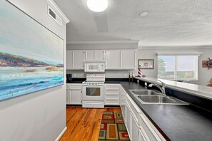 A kitchen with white cabinets, a microwave, an oven, a sink, and a wooden floor. - Direct Oceanfront Condo in the Heart of The Village. (St. Simons Island)