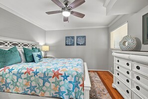 A bedroom with a bed, a dresser, a ceiling fan, and wall art. - Direct Oceanfront Condo in the Heart of The Village. (St. Simons Island)