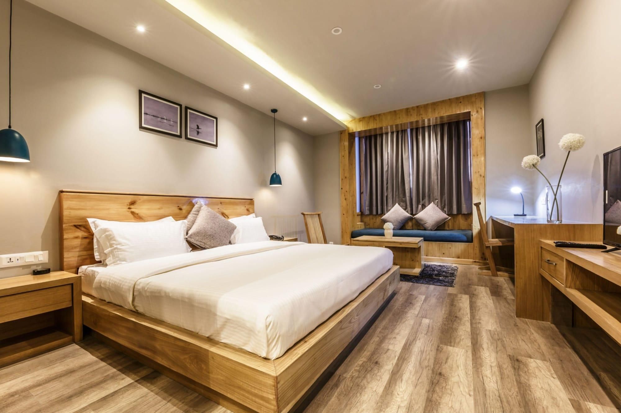 A modern hotel room with a wooden bed, a desk, and a seating area with a view of the outdoors.