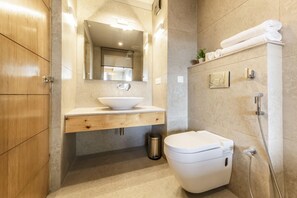 A modern bathroom with a wooden vanity, a white sink, a toilet, and a shower area. - The Bodhi Tree (Leh)