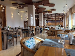 A restaurant interior with wooden furniture, pendant lighting, and a central decorative wall. - The Bodhi Tree (Leh)
