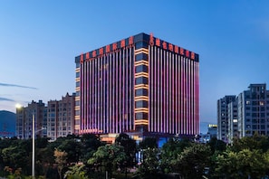 Um edifício alto de hotel com linhas verticais e sinalização iluminada.